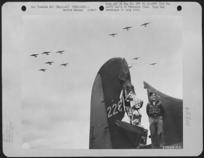 Battle Damage > T/Sgt. Harris Goldberg of Brookline, Mass., Boeing B-17 tail gunner, stands beside the tail of his plane which was hit by 20 mm. cannon fire while on a mission over enemy territory. A formation of Boeing B-17s may be seen flying overhead. Thurleigh