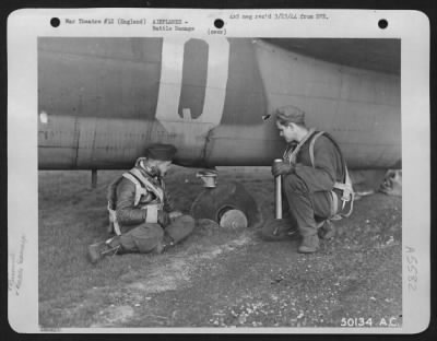 Thumbnail for Battle Damage > ENGLAND-Flak punctured tail wheel tire over Berlin but didn't prevent pilot making a good landing at home base. Shown examining the wheel are 2nd Lt. Homer Glass, Chicago (left) and Sgt. Megchelsen, Ainsworth, Iowa. A flak hole in fuselage can be