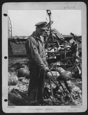 Battle Damage > M/Sgt. George Clevanik of Irwin, Pa., in midst of strewn wreckage of the Consolidated B24 Liberator "Vadie Raye", on which he was engineer and gunner, points to spot where he was suspended from catwalk and dragged along runway as the blazing ship