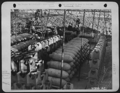 Thumbnail for General > England-Ordnance crew under supervision of Capt. Harry Faulkner, Jersey City, N.J., loads 500 lb. high explosive bombs on to trailer with aid of crane. The revetment is covered by camouflage netting and rows of tail fins can be seen between