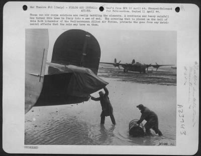 Consolidated > These two air corps soldiers are really battling the elements. A continous and heavy rainfall has turned this base in Italy into a sea of mud. The covering that is placed on the tail of this B-24 Liberator of the Mediterranean Allied Air Forces