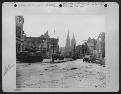 Consolidated > Tanks of the U.S. Third Armored Division roll through a debris lined street in the city of Cologne, Germany. Twin spires of the famous Cathedral loom in the background.