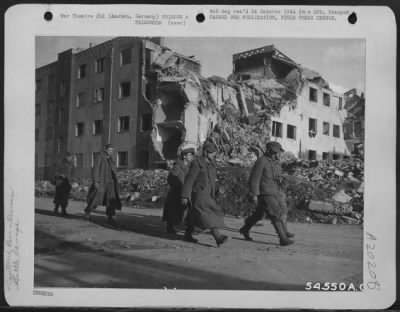 Thumbnail for Consolidated > German prisoners of war, among the first to be captured in Aachen, Germany, tramp through a street of the town on their way to a collecting point. The damaged building in the background is a sample of the results achieved by artillery pounding and