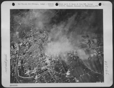 Thumbnail for Consolidated > B-25 Mitchell Bombers of the 12th AF recently hit the important railroad yards at Foligno, Italy. The thousand-pound bombs dropped by the Mitchells leave a thick pall of smoke over the entire target area as many direct hits are scored. The