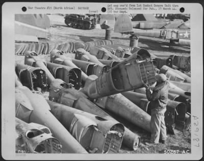 Thumbnail for Consolidated > North Africa-This group of Tail Booms, removed from various speedy P-38 fighters similar to one shown in background, have each seen action in aerial combat, but after thorough examination, parts or entire booms will again be fitted to the after