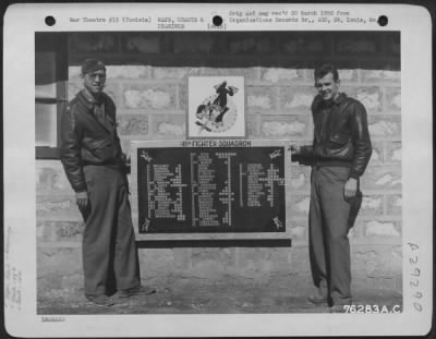 Thumbnail for Consolidated > Two Members Of The 48Th Fighter Squadron, 14Th Fighter Group, Stationed At An Air Base Somewhere In Tunisia, Proudly Display A Poster Which Proclaims The Score Of The Units Fighter Pilots.  1943.