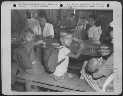 Thumbnail for Consolidated > Prisoners liberated from a prison camp in Manila, Luzon, Philippine Islands, eat their first meal away from the Japs in three years. Knapsacks worn by the children were made by their mother to carry all of their belongings.