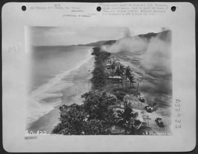 Thumbnail for Consolidated > Hit: One fuel truck, which catches fire as 5th Air Force strafe the strip at Wewak, New Guinea. Camouflage awnings for planes beneath trees only seem to make them more conspicuous here.