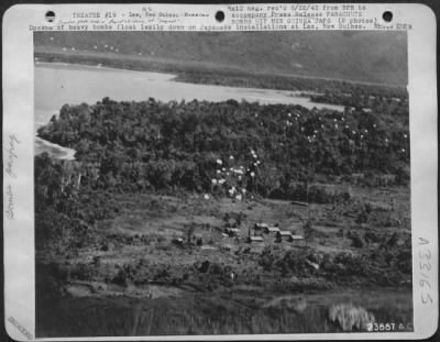 Thumbnail for Consolidated > Dozens of heavy bombs float lazily down on Japanese installations at Lae, New Guinea. Spots in middle right of picture, and in upper left, show still more bombs, which will explode a few feet above the ground, or on contact with terrific and