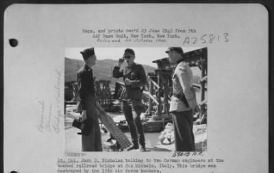 Consolidated > Lt. Col. Jack D. Nicholas talking to two German engineers at the bombed railroad bridge at San Michele, Italy. This bridge was destroyed by the 15th Air Force bombers.