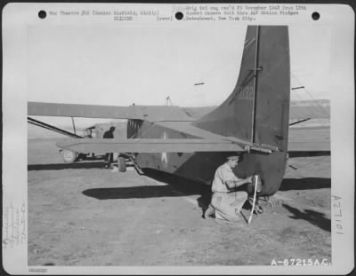 Thumbnail for Consolidated > A parachute rigger attaches parachute arrestor to a glider participating in the 52nd Troop Carrier Wing maneuvers at Comiso Airfield in Sicily in 1943. Note the cords from the chute; they are attached to the ring which is built out just behind the