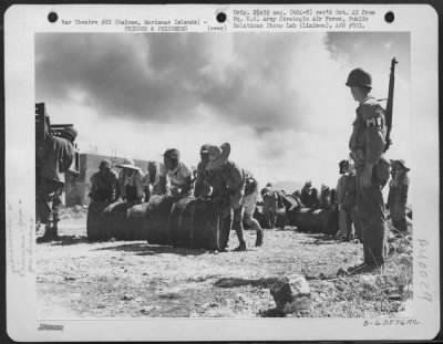 Thumbnail for Consolidated > Japanese Soliders And Civilian Prisoners Of War Rolling And Stacking Gasoline Drums At A Supply Dump While Pvt. William E. Regan Of 170-01 91St Road, Woodhaven, Long Island, New York, Stands Guard.  Saipan, Marianas Islands, 29 June 1944.